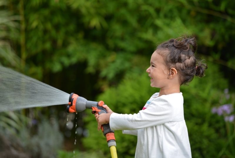 girl with hearing aids spraying a garden hose